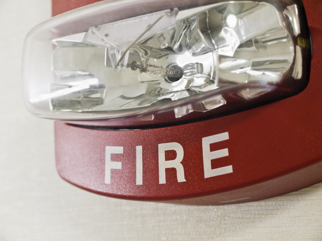 Close-up of red fire alarm with strobe light on a white wall.